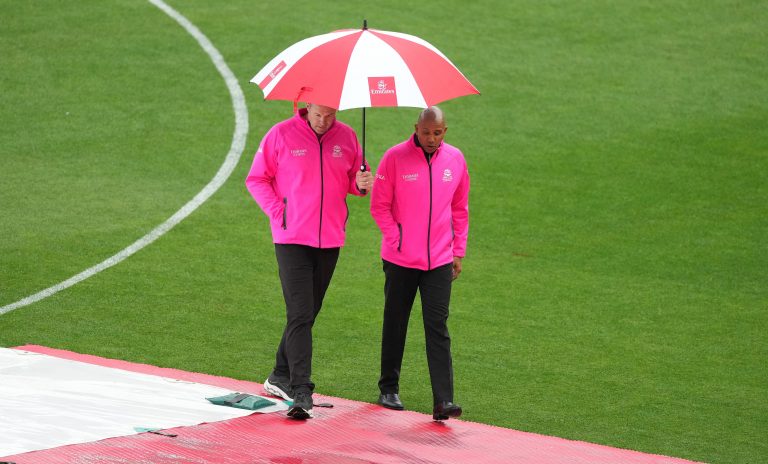 Umpires Chris Brown, left, and Joel Wilson shelter under an umbrella while inspecting the outfield